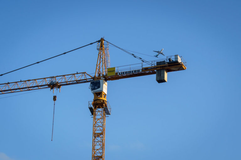 a Liebherr branded construction crane with an airplane flying far above it