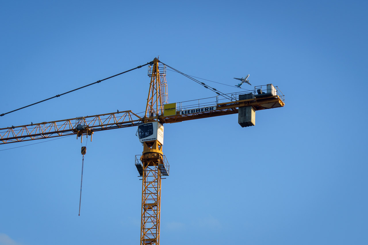a Liebherr branded construction crane with an airplane flying far above it