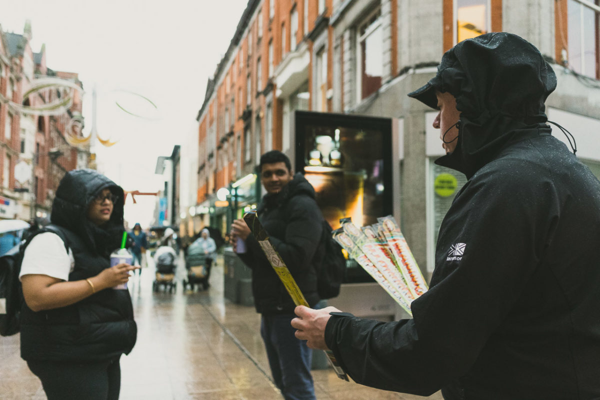 A man selling sparklers on Halloween on Henry Street, Dublin. Two people in the background being polite and listening to him.