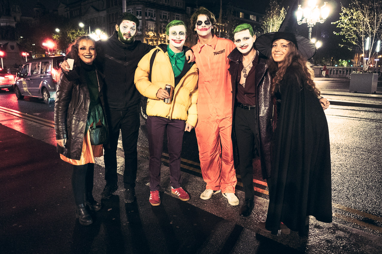 A group shot of several young men dressed as Joker with two witches, one on either side, on Halloween night