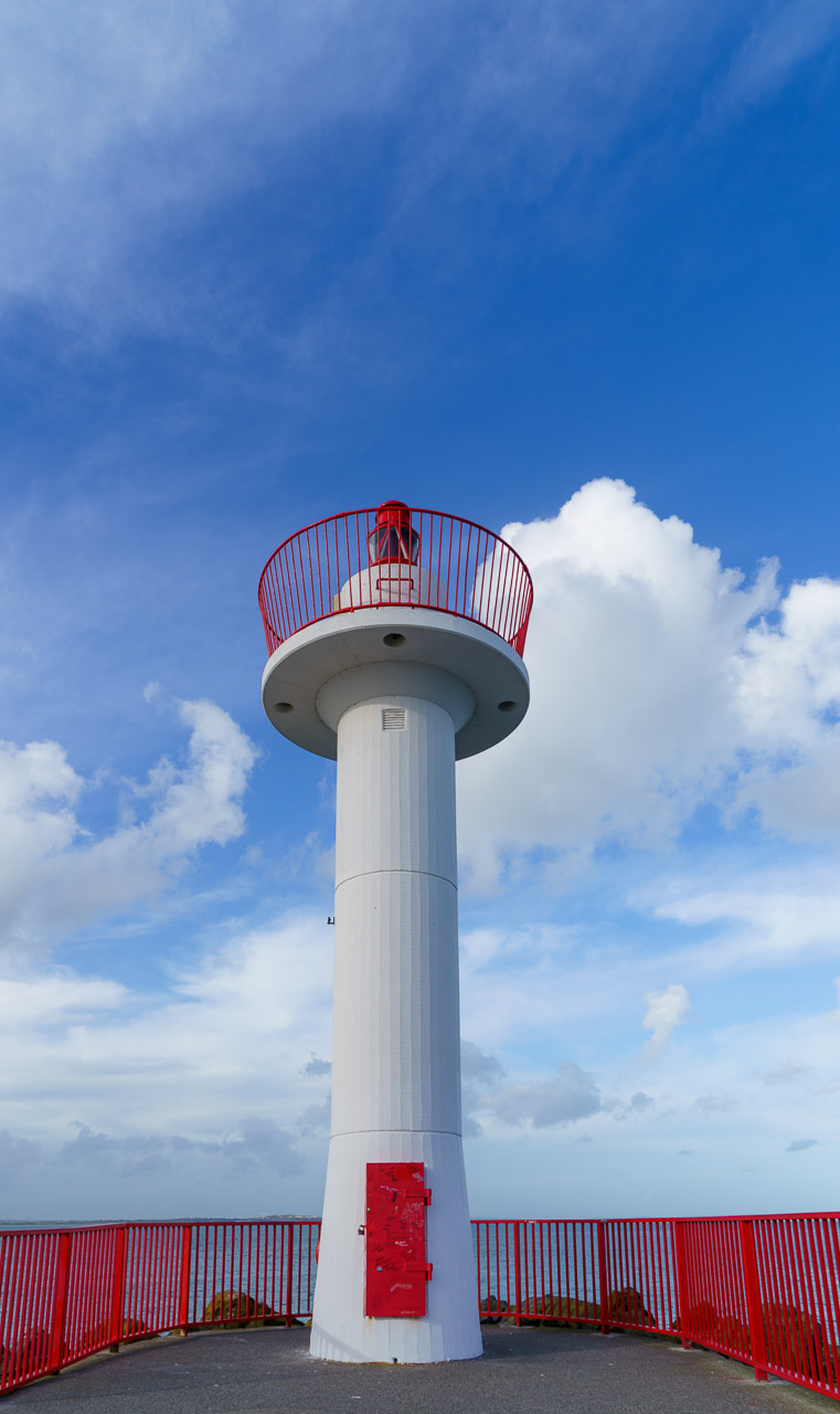 A thick pole with lights at the top. Blue skies and fluffy clouds behind it.