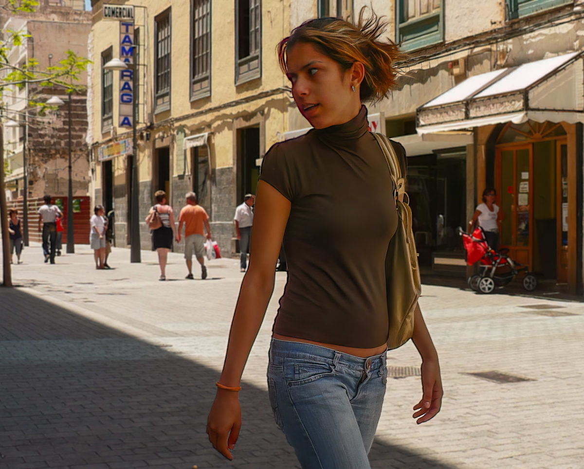 A woman walking along a street looking over her shoulder at something that has caught her attention.