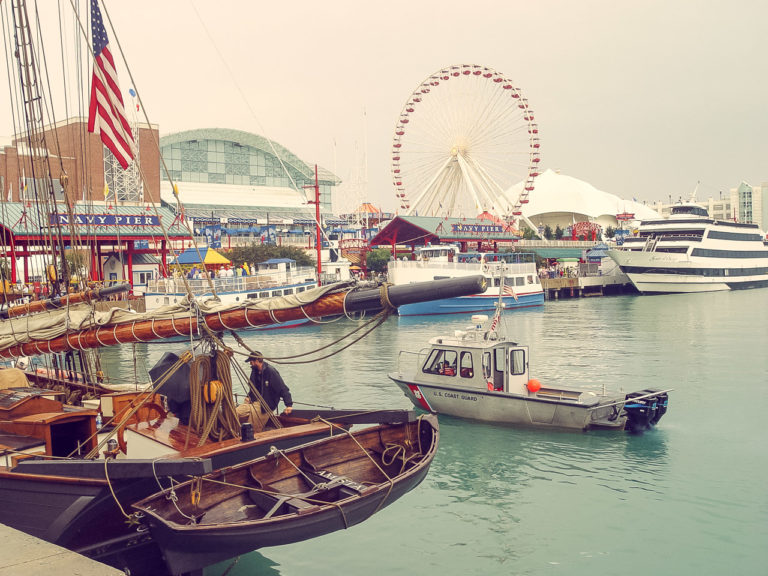 Lots of boats seen in the water at Navy Pier in Chicago. A Ferris Wheel can be seen in the background.