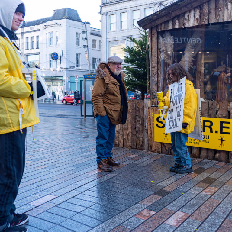 Charity collectors and a man digging through his pocket for change.