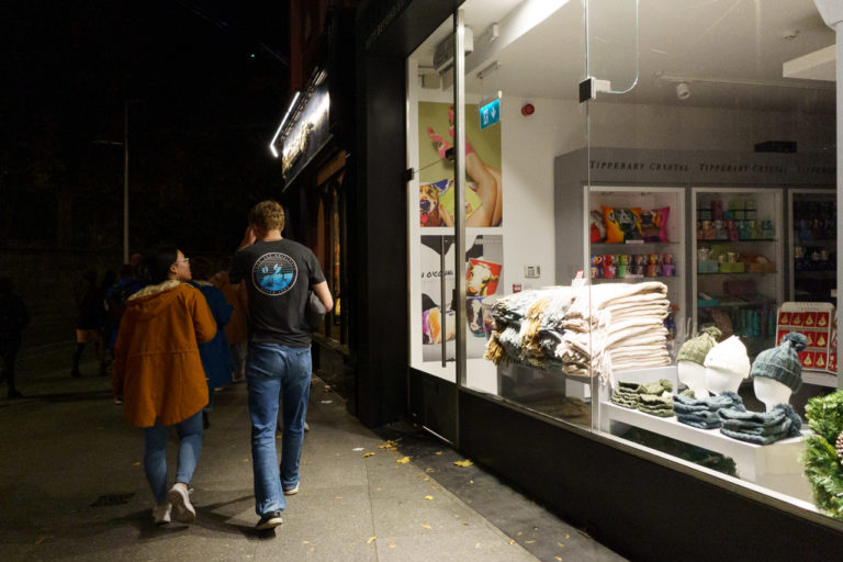 A woman and a man walk past a shop selling wool hats and scarfs.