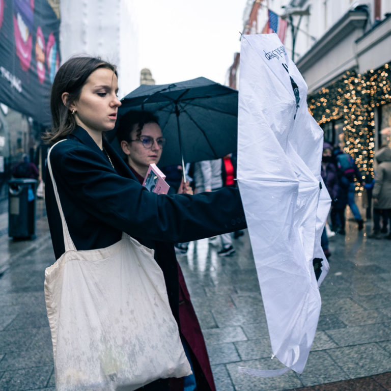 A woman gets out her umbrella while another woman walks next to her with her umbrella open