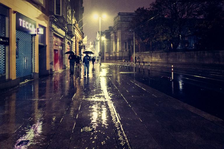 A rainy, wet street in Dublin at night. Two people walking towards me with umbrellas.