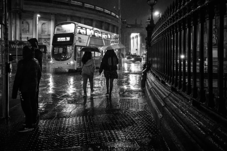 Two women walk past the entrance to Trinity with umbrellas while it rained.