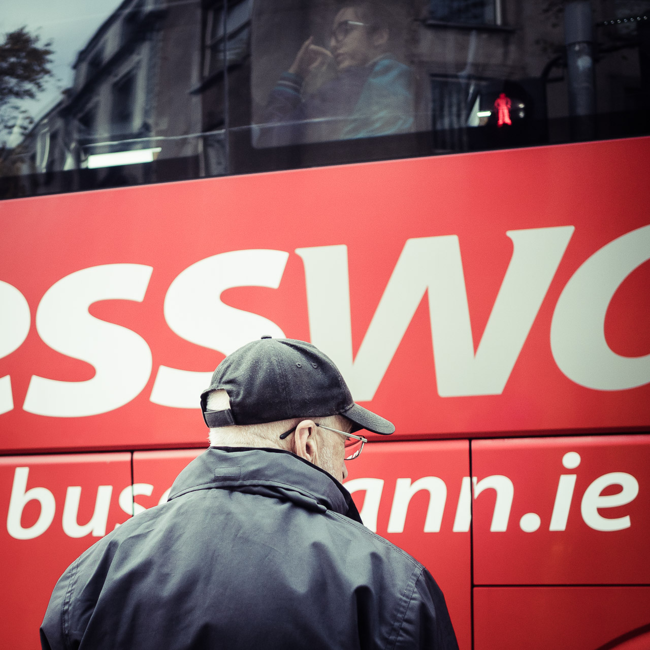 A bus on the road and a man looks to the right. A woman in the bus.