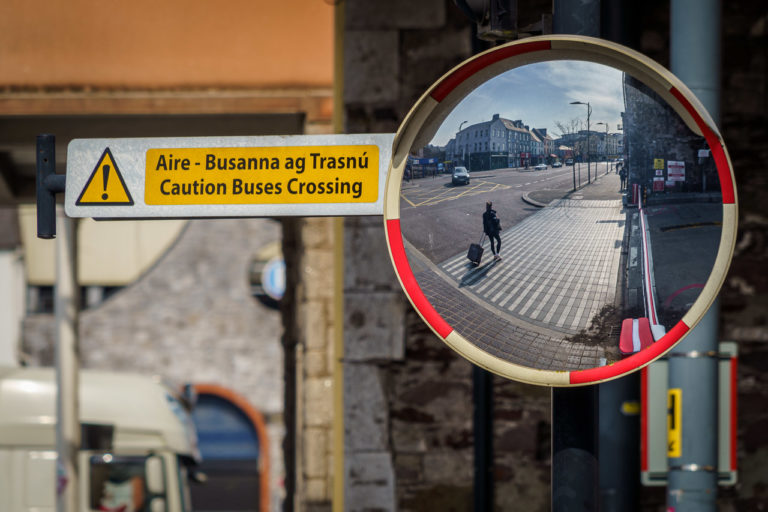 A long figure is seen walking on a pavement in a convex mirror.