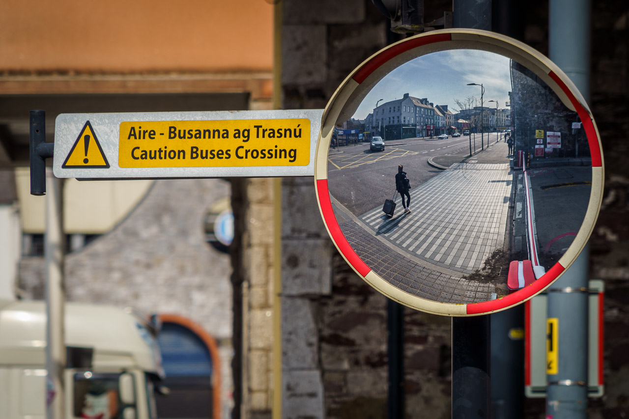 A long figure is seen walking on a pavement in a convex mirror.
