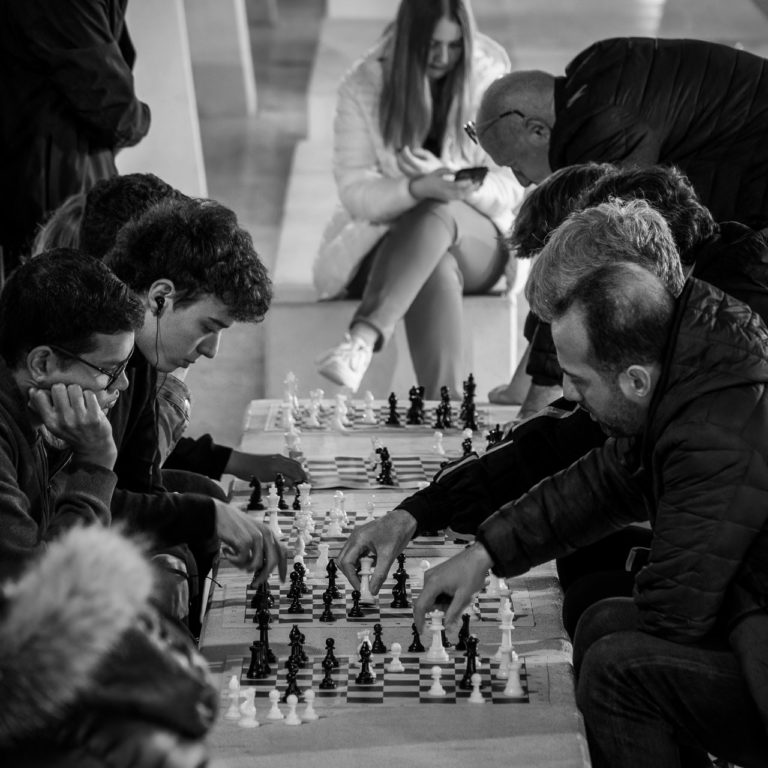 Chess players in Malaga concentrate on their game. A young woman in the background checks her phone.