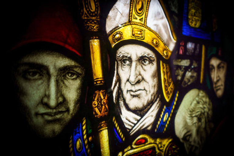 A stained glass picture of 4 men, one dressed the garbs of a Christian bishop.