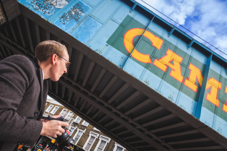 A photographer in Camden Town, London. In the background is the North London Line bridge over Chalk Farm Road.