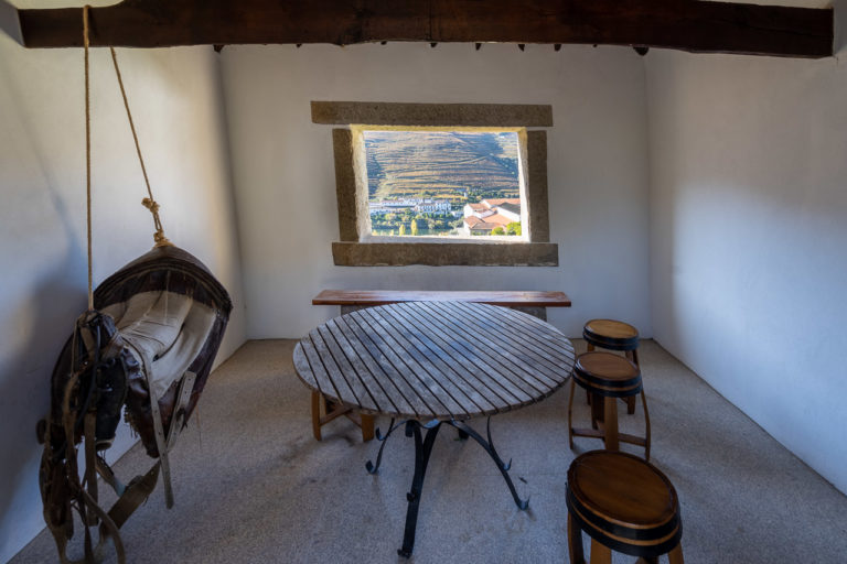 A small room looks out on the Douro Valley. Inside the room are a table, some stools and what looks like a saddle hanging from the ceiling