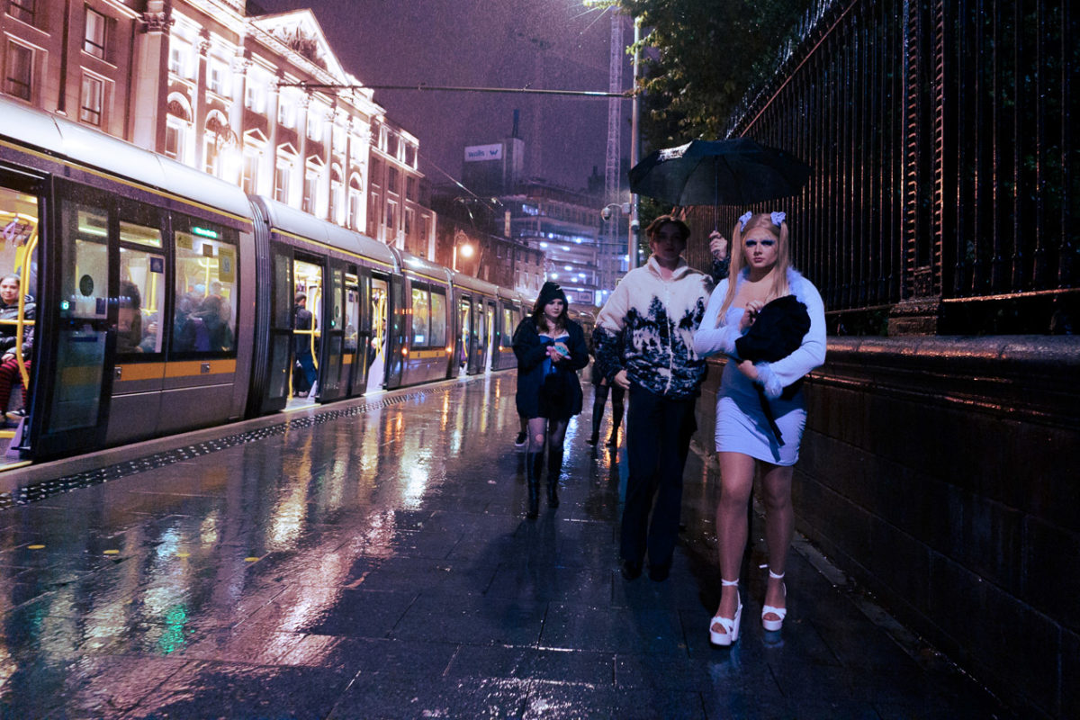 A group of young people heading out for the night in Dublin on a gloomy, rainy evening. The Luas can be seen on the left.