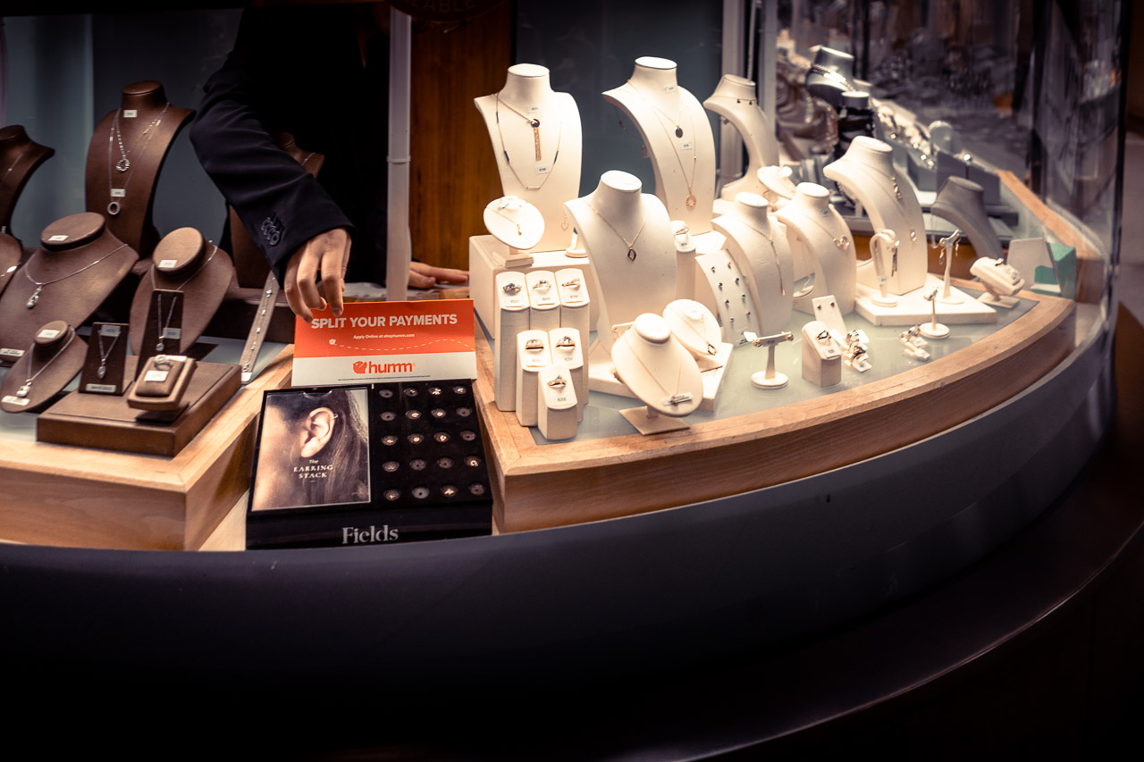 The display in the front window of a jewellery store. A hand reaches out from behind to move a sign that says, "Split Your Payments".
