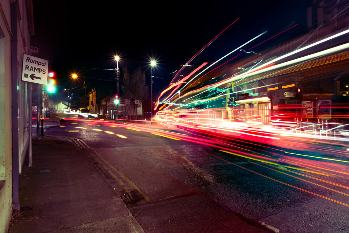 The lights of passing cars and buses streak into the distance on this busy junction at night.