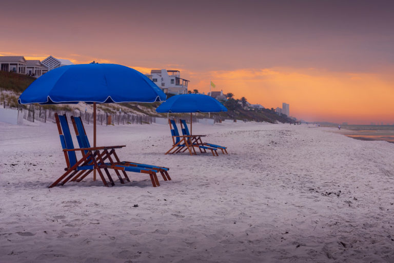 Blue parasols provide shade for beach chairs on the beach by Seaside in Florida as the sun rises