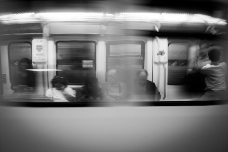 People on a subway train. Looking at phones or talking, standing, seated.