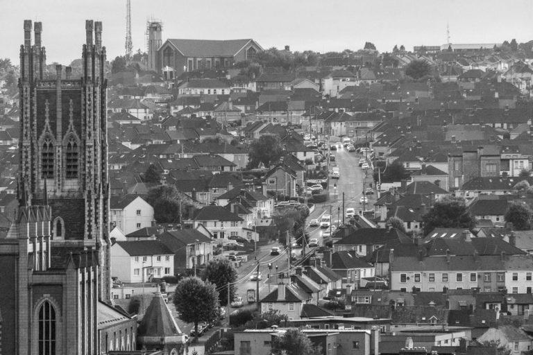 The view from Bell's Field, Cork looking over towards The Cathedral Of St Mary & St Anne, on towards Cathedral Road and up the hill to The Church of the Ascension. Cars on the road and lots of houses visible too.