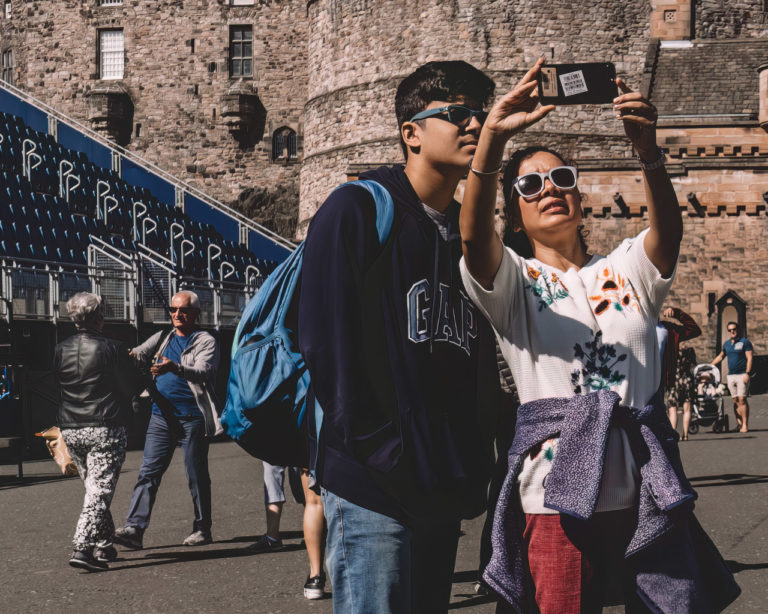 People taking selfies in Edinburgh Castle while in the background an older couple greet each other.