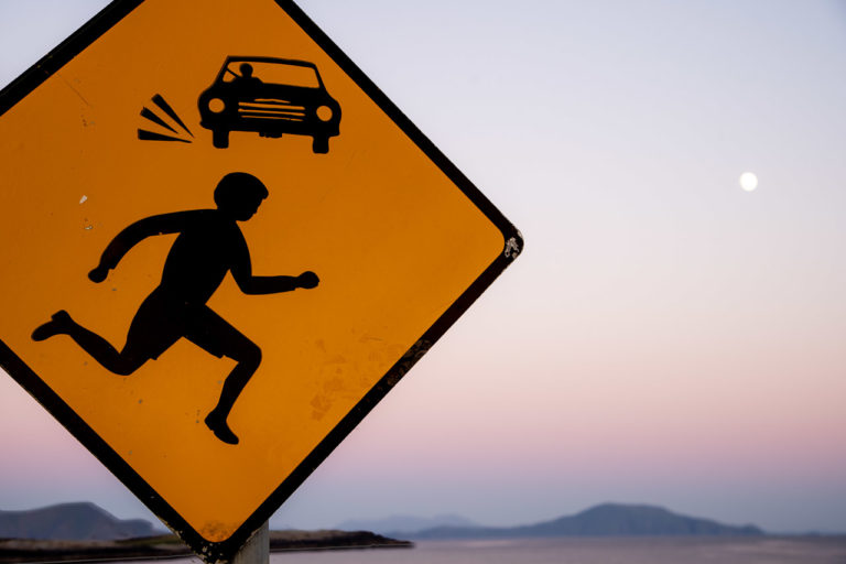 A yellow sign warns car drivers that children are running around, while the Moon shines down out of the early evening sky