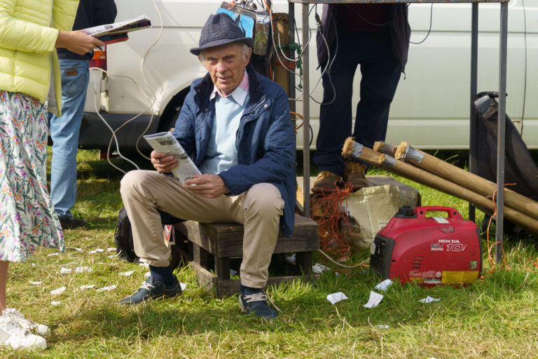 A man sitting down on a box, checking the horses at a race meet.