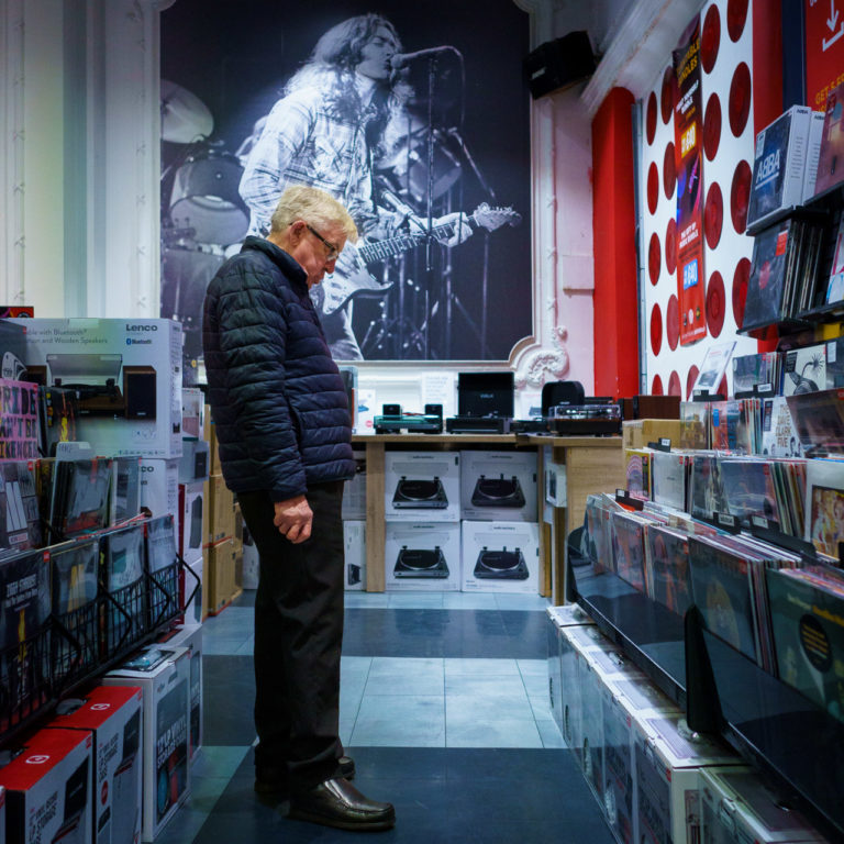 A man looking at records in a music store with a big poster of Rory Gallagher on the wall behind