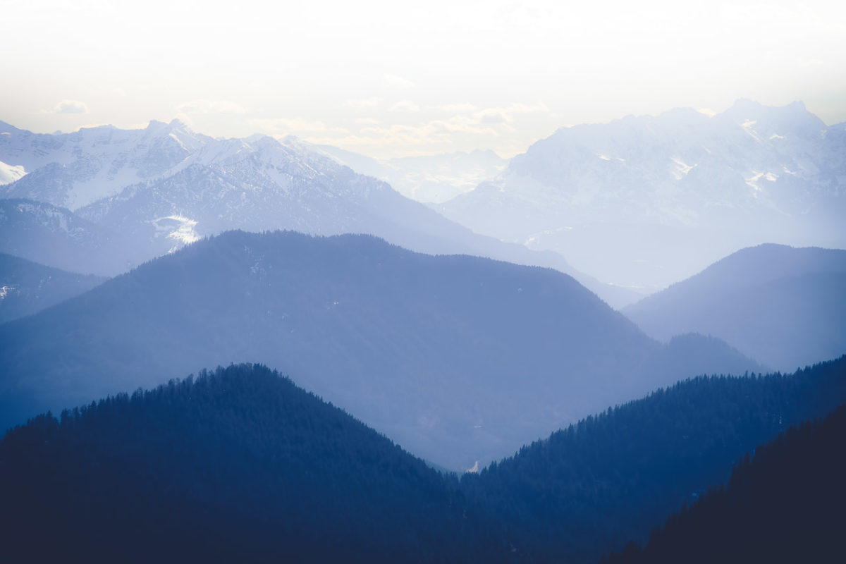 Mountains in the haze with forests and snow on them.