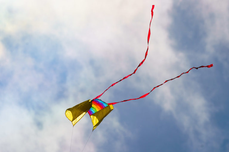 A kite flying in the sky. It's a colourful two string one with red ribbons flying out the back