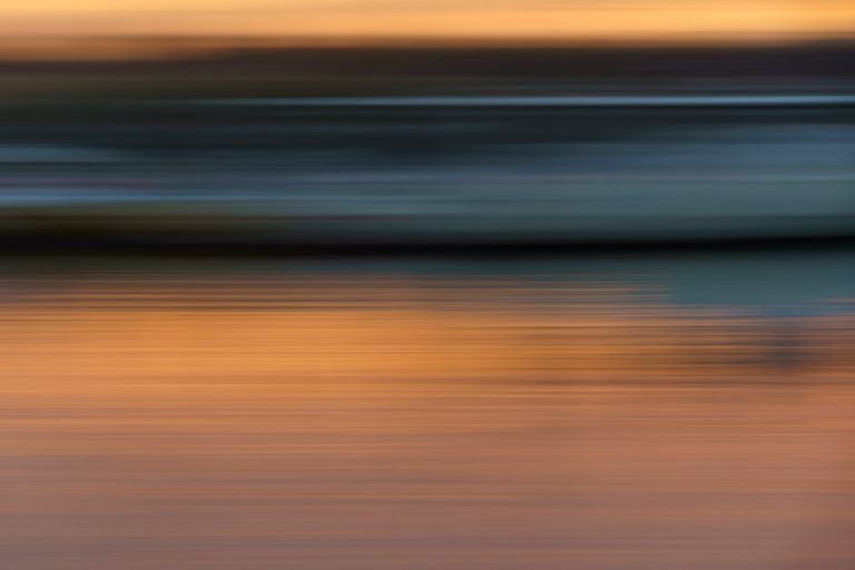 Streaks of colour in a sunset photo made by moving the camera left to right. The colours go from a dark smudgy grey and blue to vibrant orange.