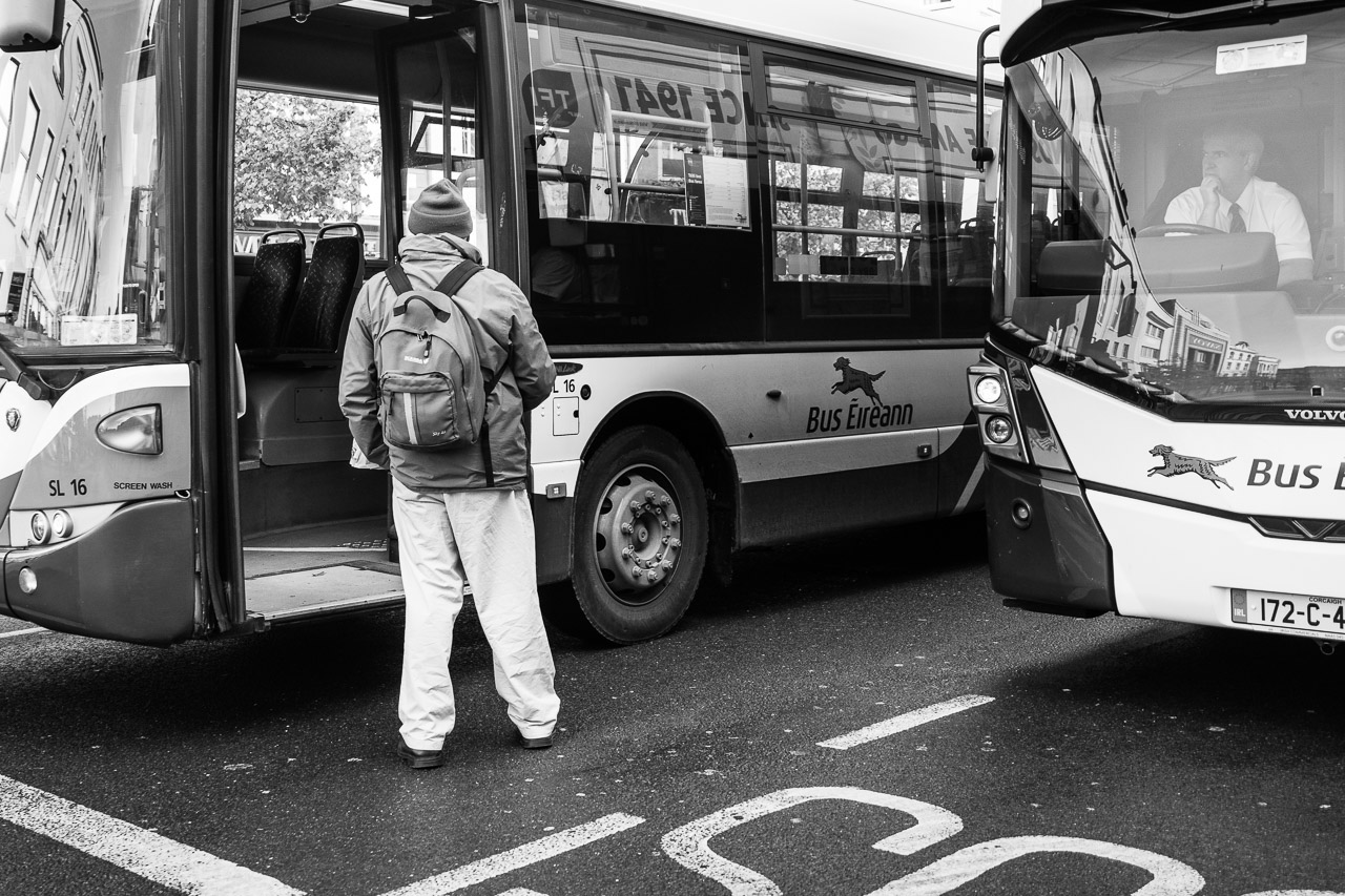A man stands outside a bus waiting to get on. He's watched intently by a bus driver in another bus beside it.