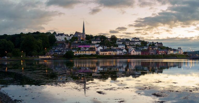 Crosshaven town reflected in the water of the harbour. Clouds and the sky are yellow/orange from the setting sun.