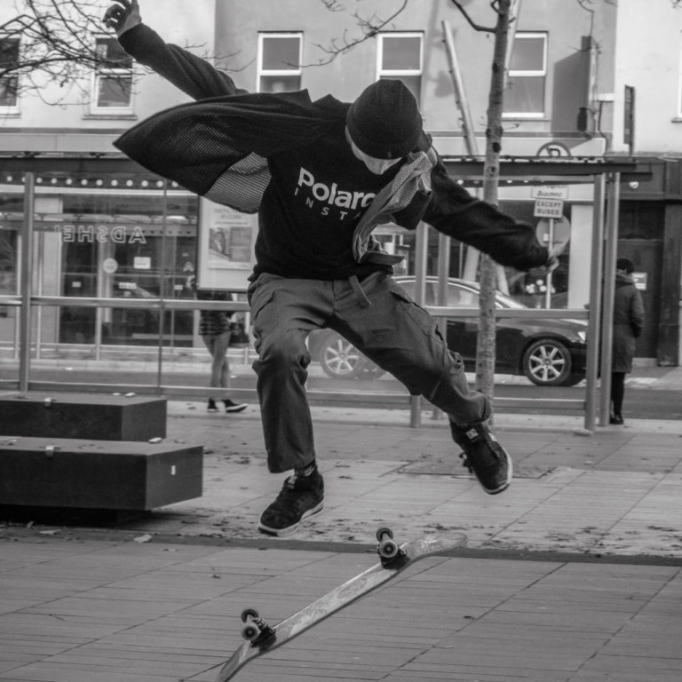 A skateboarder jumps in the air in a black and white photo on a street.