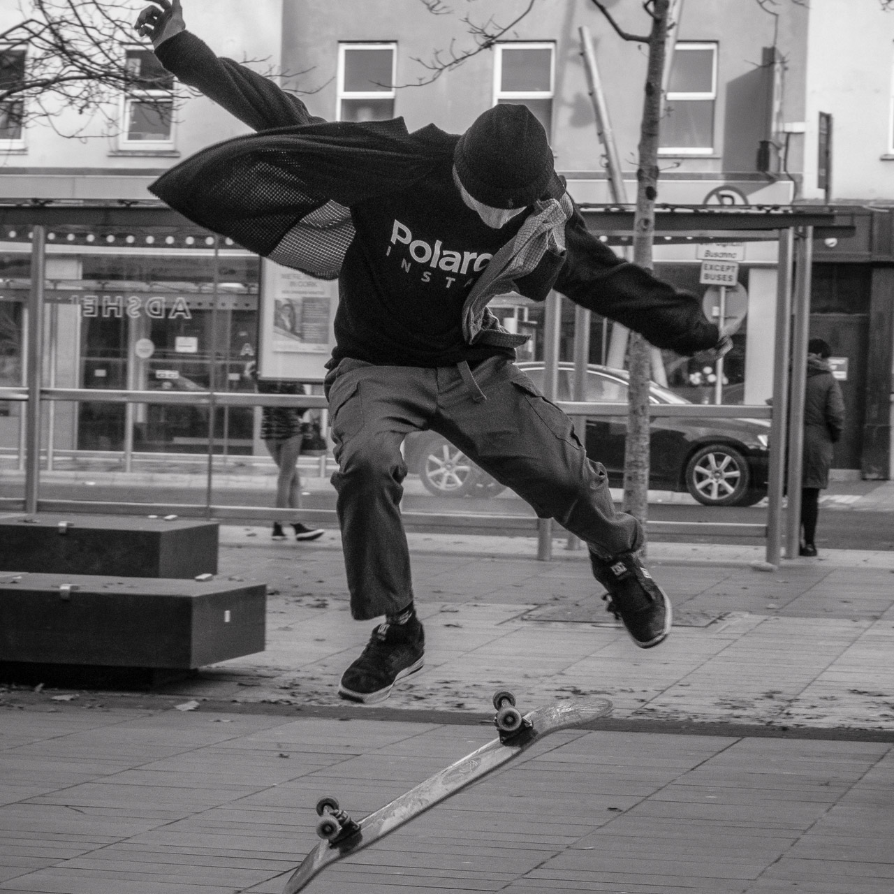 A skateboarder jumps in the air in a black and white photo on a street.