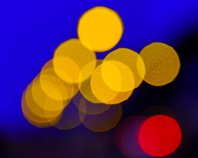 The out of focus lights of Youghal on a dark evening, just after sunset. The red brake light of a vehicle lights up the bottom right of the photo.