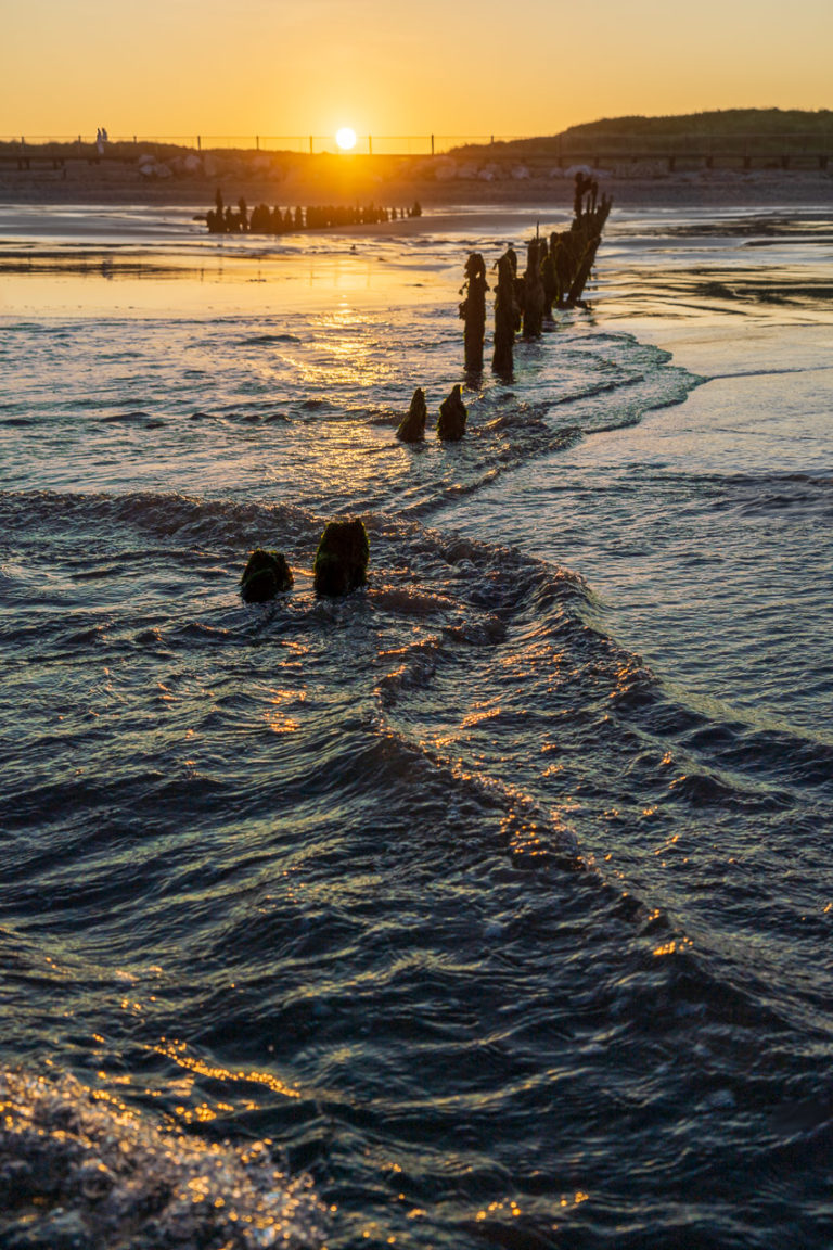 Waves roll in over the groynes in Youghal as the sun sets
