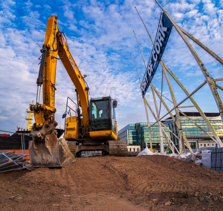The "PORT OF CORK" sign looms over construction equipment and a big pile of earth