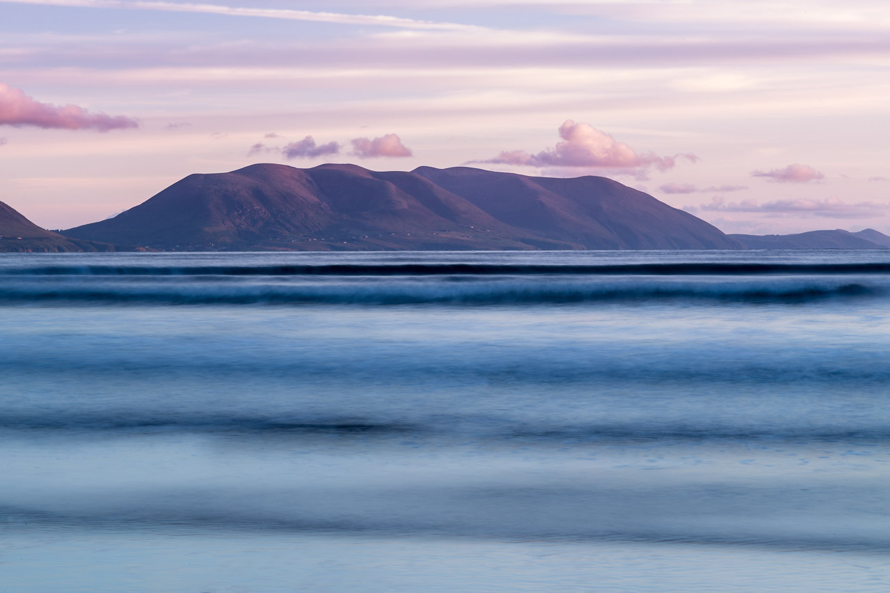 Far away hills lit up by the setting sun with ephemeral waves lapping the shore