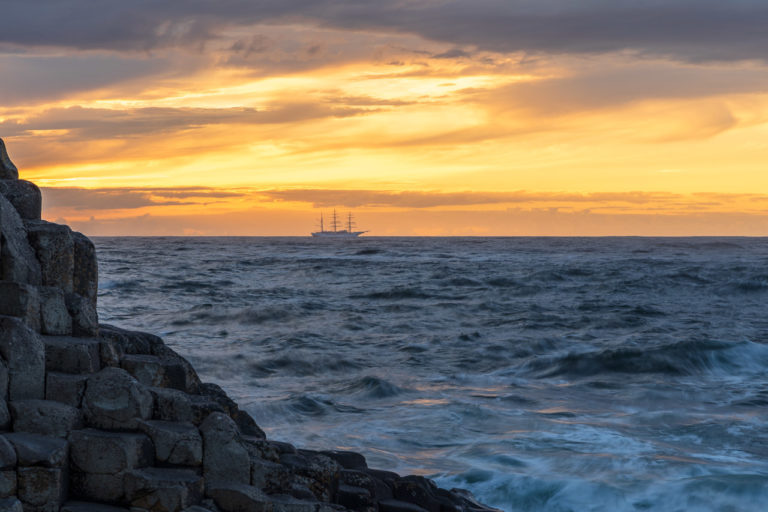 A boat sailing past on the horizon with the rocks of The Giant's Causeway
