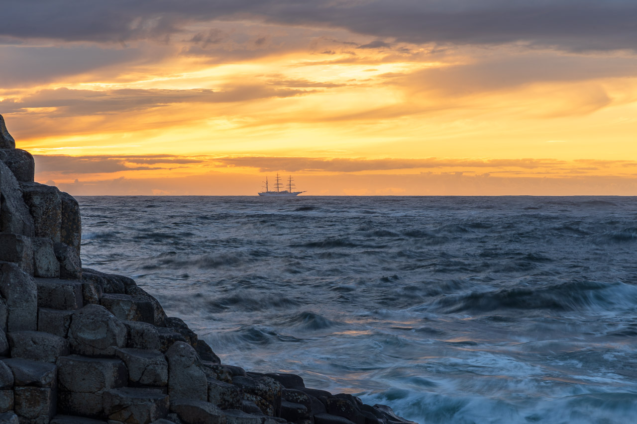 A boat sailing past on the horizon with the rocks of The Giant's Causeway