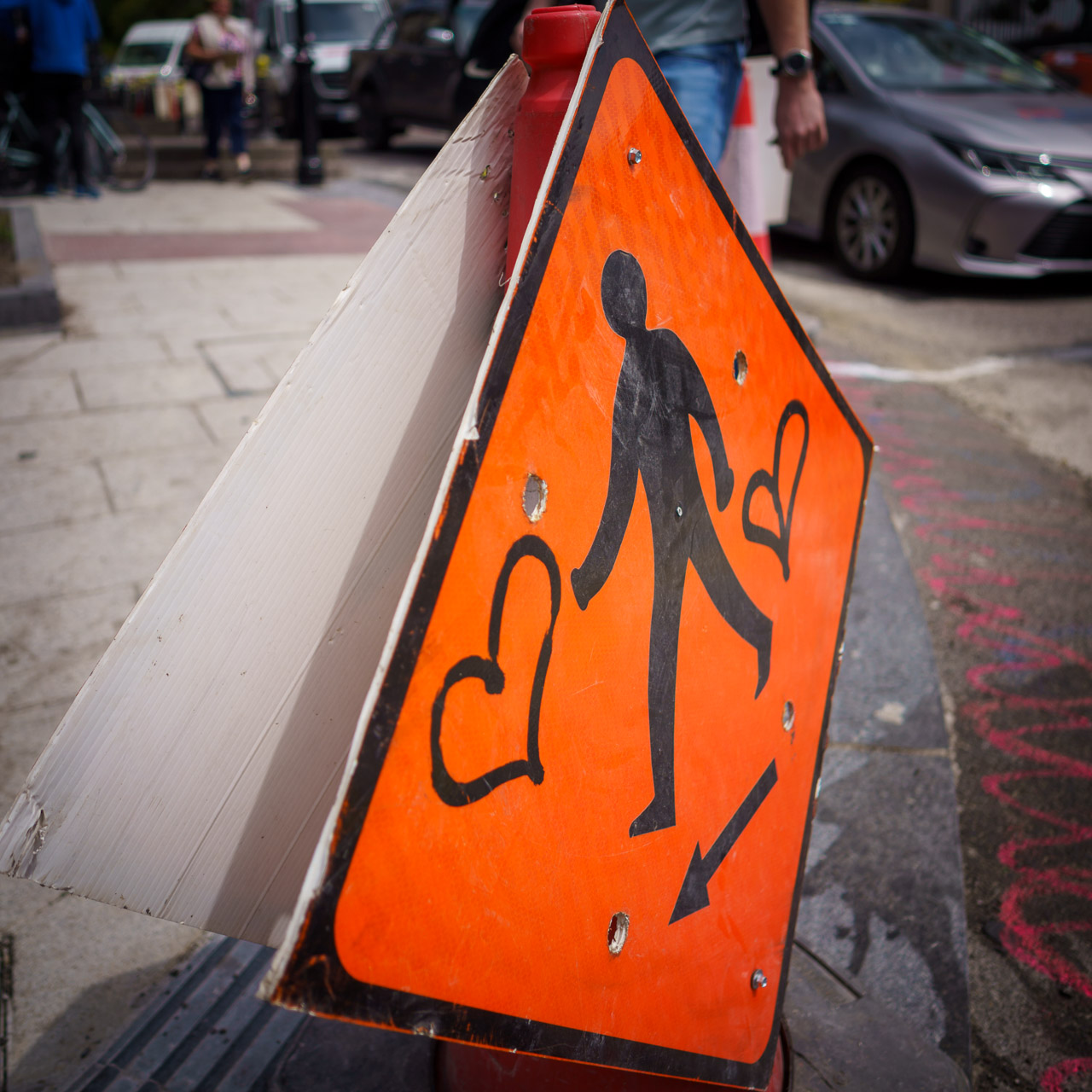 A bollard with a sign showing a man walking and an arrow pointing left. Two love hearts surround the man.