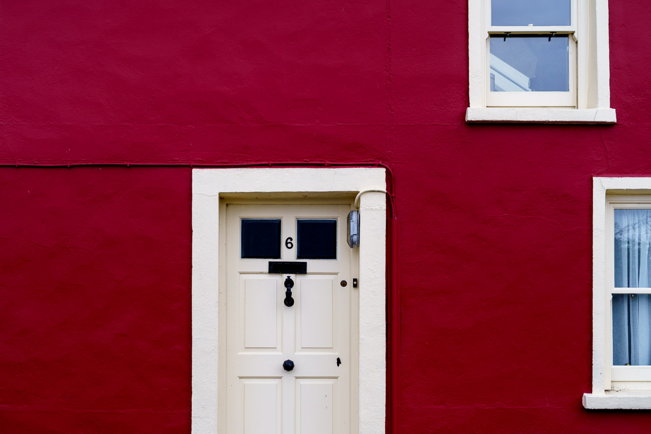 The lovely deep red of a house with the number 6 on it's door. Two windows can partially be seen above and to the right of the door.