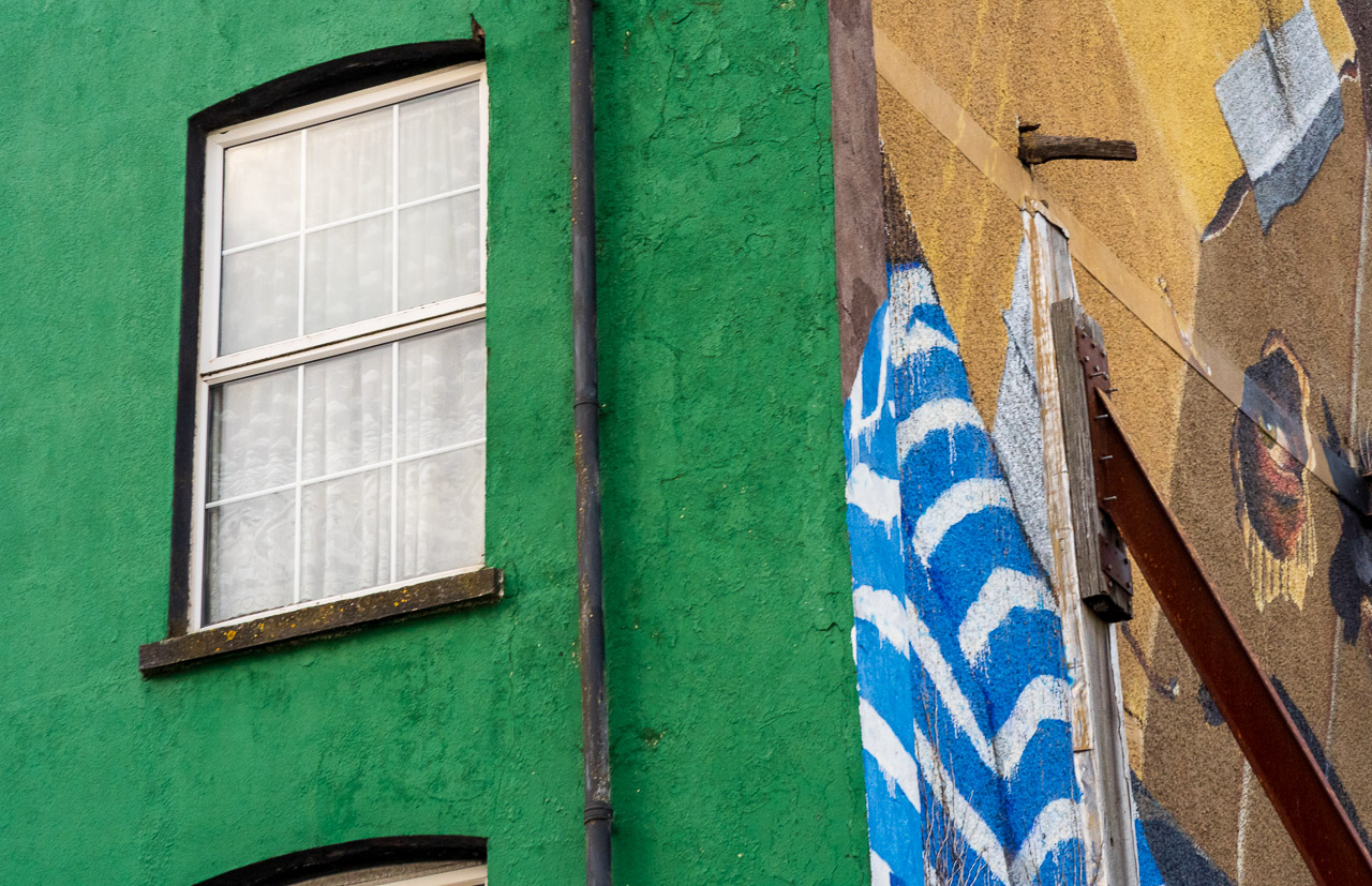 A mural on the side of a building shows a person with an Amazon box over their head. An eye looks sideways out of the box, looking at the window on the left of the photo.
