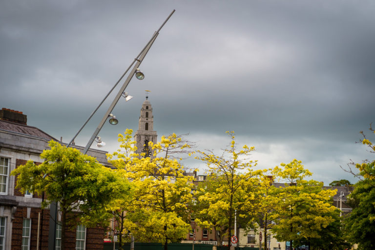 Trees, buildings and street lighting while in the background is the steeple of St. Anne's Church or Shandon Bells.