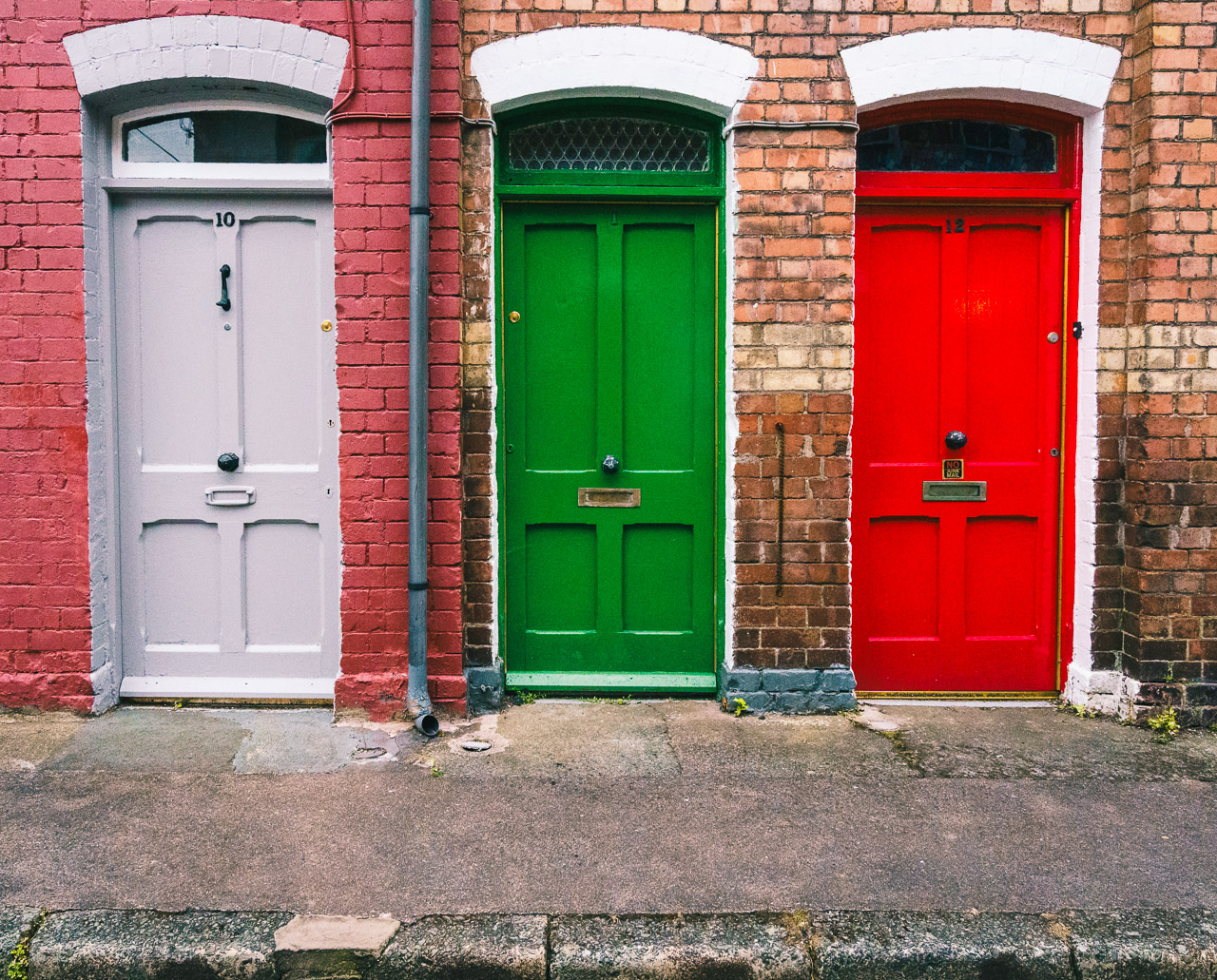 3 doors, mauve, green and red on a street.