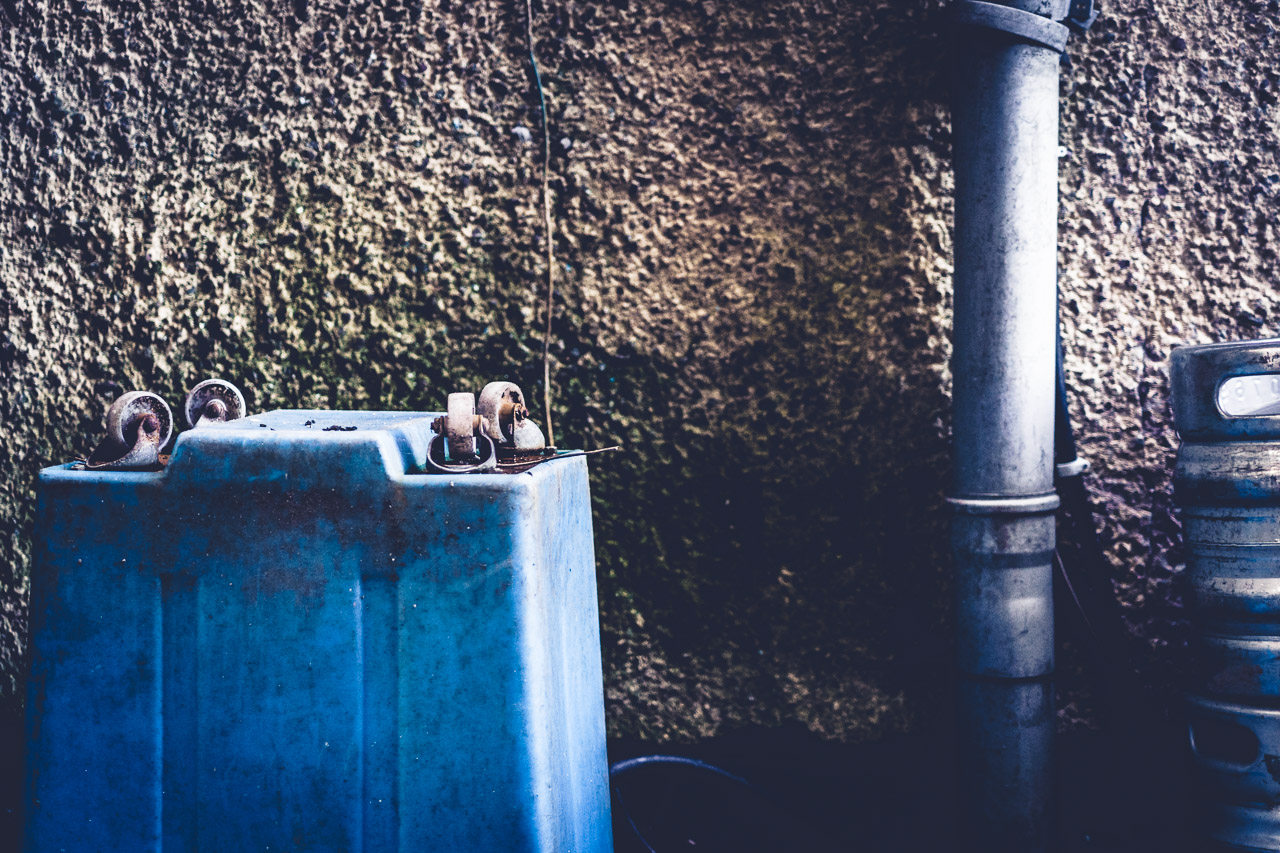 The wheels on an upside down container are useless, not touching anything. A drain pipe and the side of beer kegs are visible too in this gritty photo
