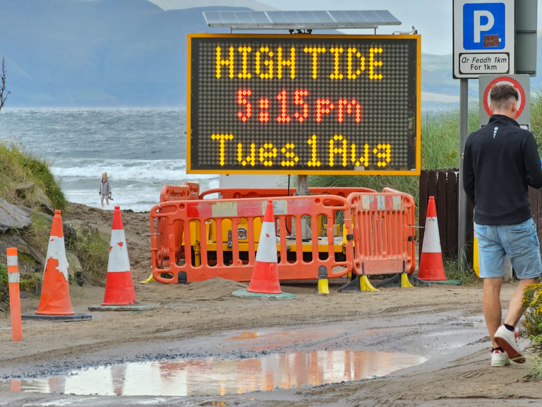 An electronic sign at a beach says, "HIGH TIDE 5:15pm Tues1Aug"