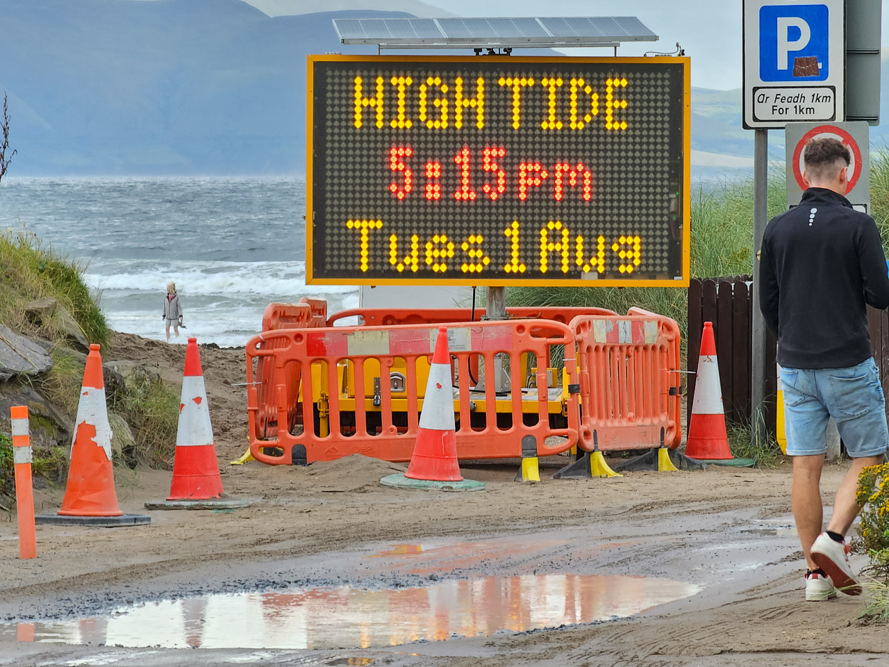 An electronic sign at a beach says, "HIGH TIDE 5:15pm Tues1Aug"